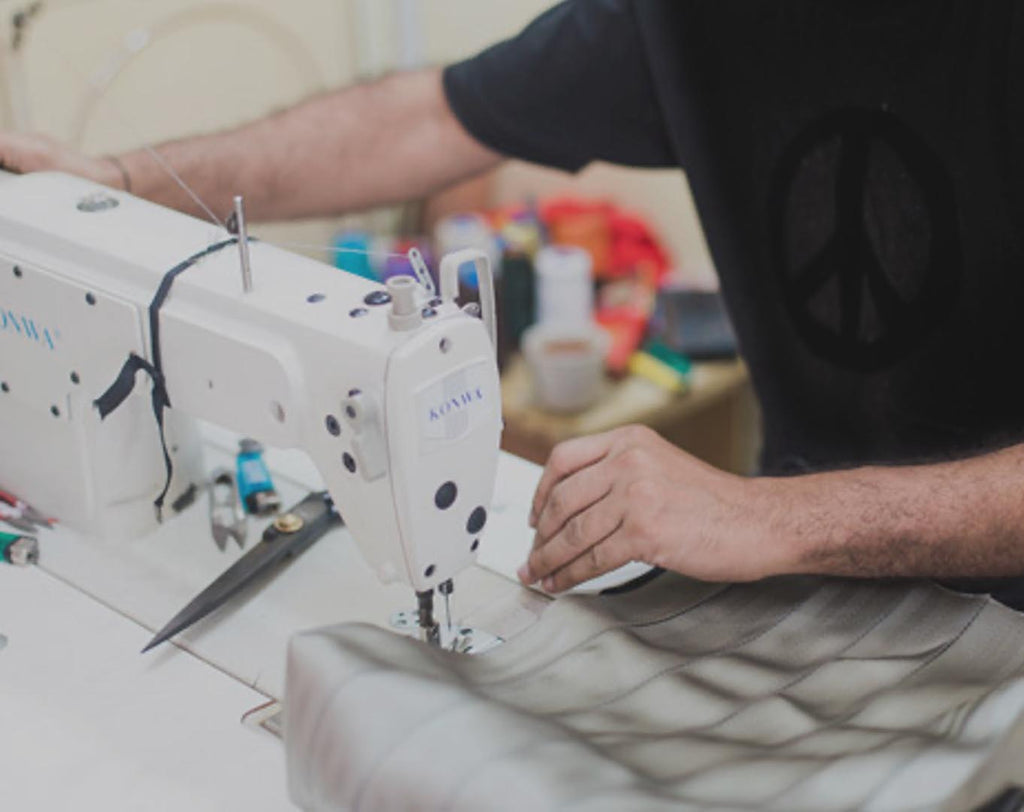 tailor stitching with a machine seatbelt pieces onto a backing fabric, forming a linear patchwork textile to make bags, plus an insert showing the taylor holding a sign stating I made your bag