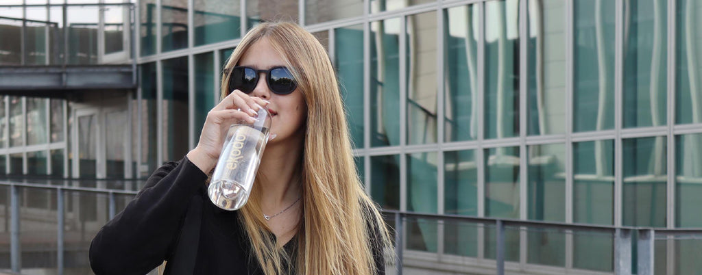 Photo of a woman drinking water from a reusable glass bottle from the brand eKodoKi, used as desktop banner