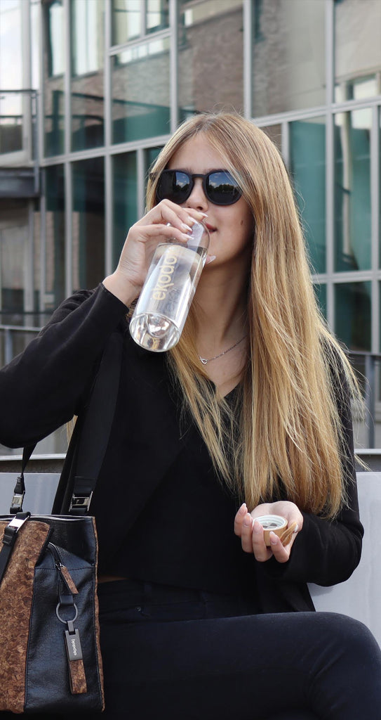 Photo of a woman drinking water from a reusable glass bottle from the brand eKodoKi, used as mobile banner