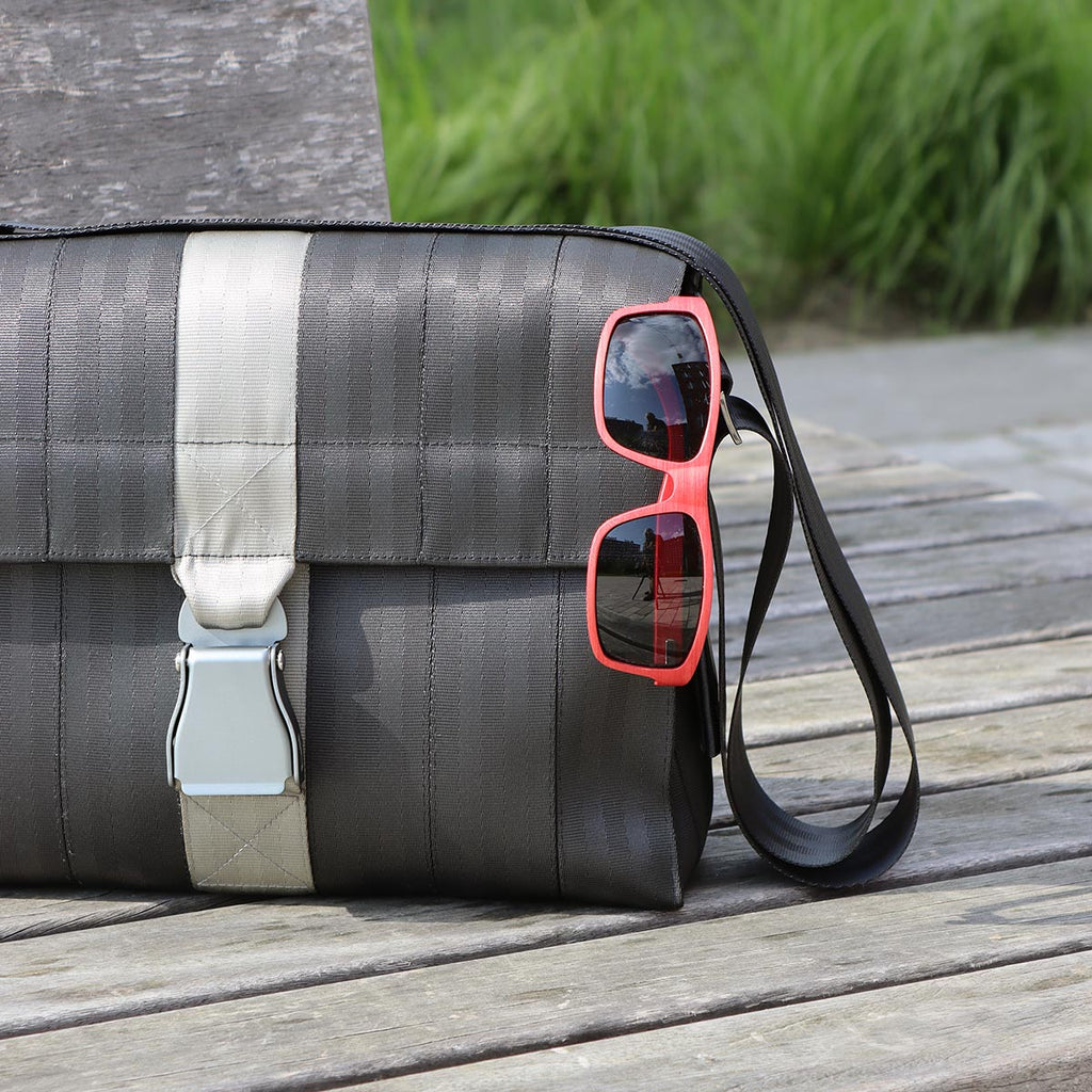 black seatbelt messenger bag size M with red wooden sunglasses hanging, both from the brand eKodoKi