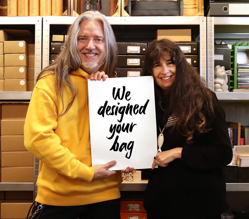 Bertrand Rigot and Marion Verbucken, in their design studio, holding together a sign stating "We Designed Your Bag"