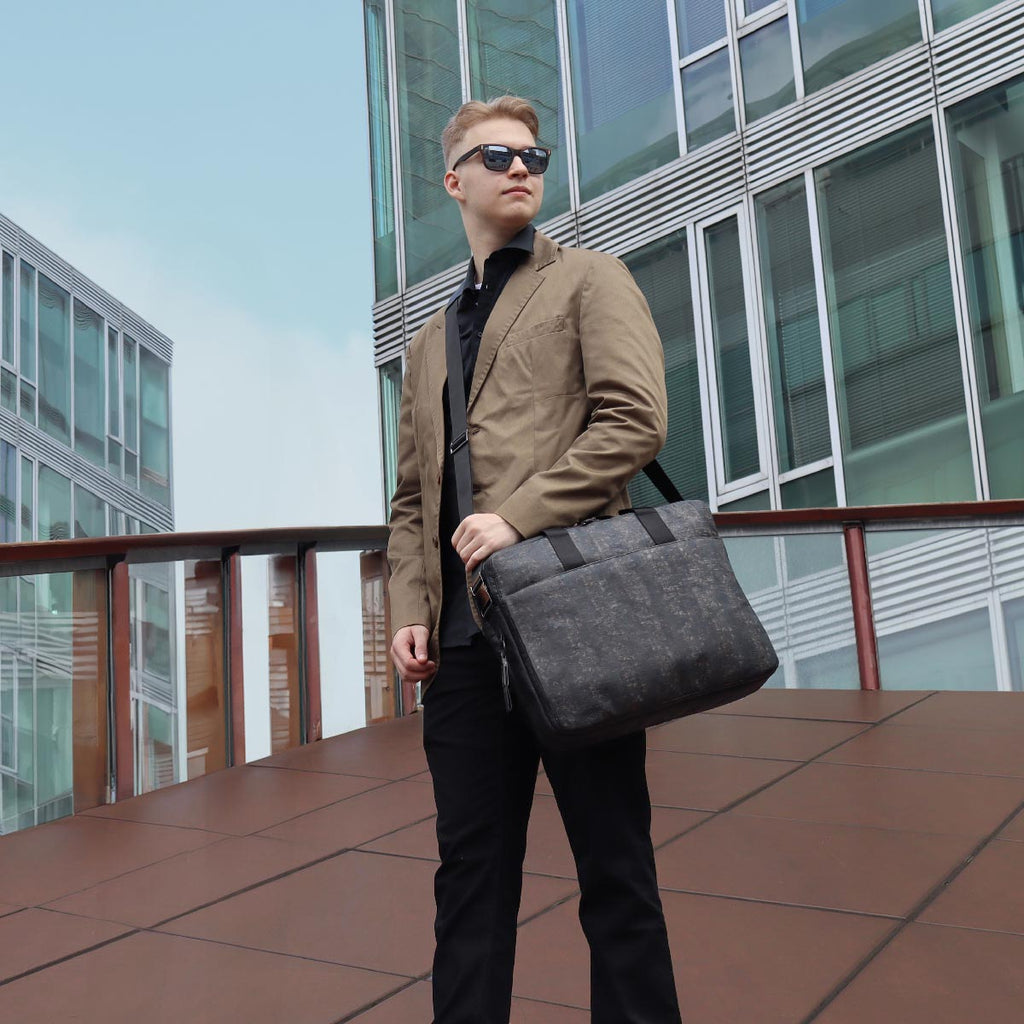 black washed cork and black hanji briefcase size L from the brand eKodoKi, carried across the shoulder by a model in suit, in front of two office buildings