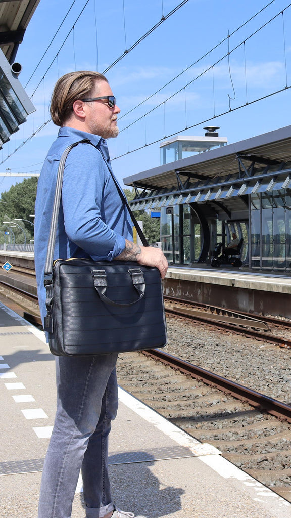 black seatbelt briefcase L on the shoulder of a male model standing on the platform of an outer train station, mobile banner, eKodoKi RE-BELT