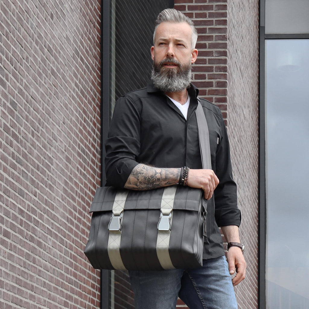 black seatbelt messenger bag L on male fashion model standing, with his arm up on the bag eKodoKi RE-BELT