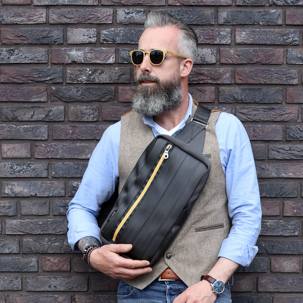 black seatbelt sling bag L on male fashion model chest standing against the wall, closed eKodoKi RE-BELT