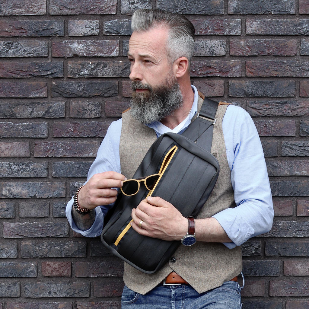 black seatbelt sling bag L on male fashion model chest standing against the wall, opened eKodoKi RE-BELT