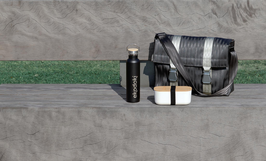 seatbelt bag, reusable bottle and lunchbox from the brand eKodoKi, on a bench, as desktop banner to illustrative example of the bundles offered by the D2C shop