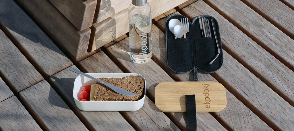 White bamboo 700ml lunchbox with food in it, next to a silver colour stainless steel travel cutlery set in its grey wool felt case, both from the brand eKodoKi, used as desktop banner