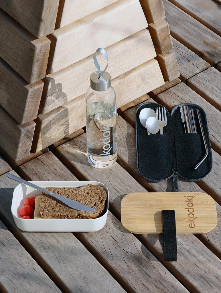 White bamboo 700ml lunchbox with food in it, next to a silver colour stainless steel travel cutlery set in its grey wool felt case, both from the brand eKodoKi, used as mobile banner
