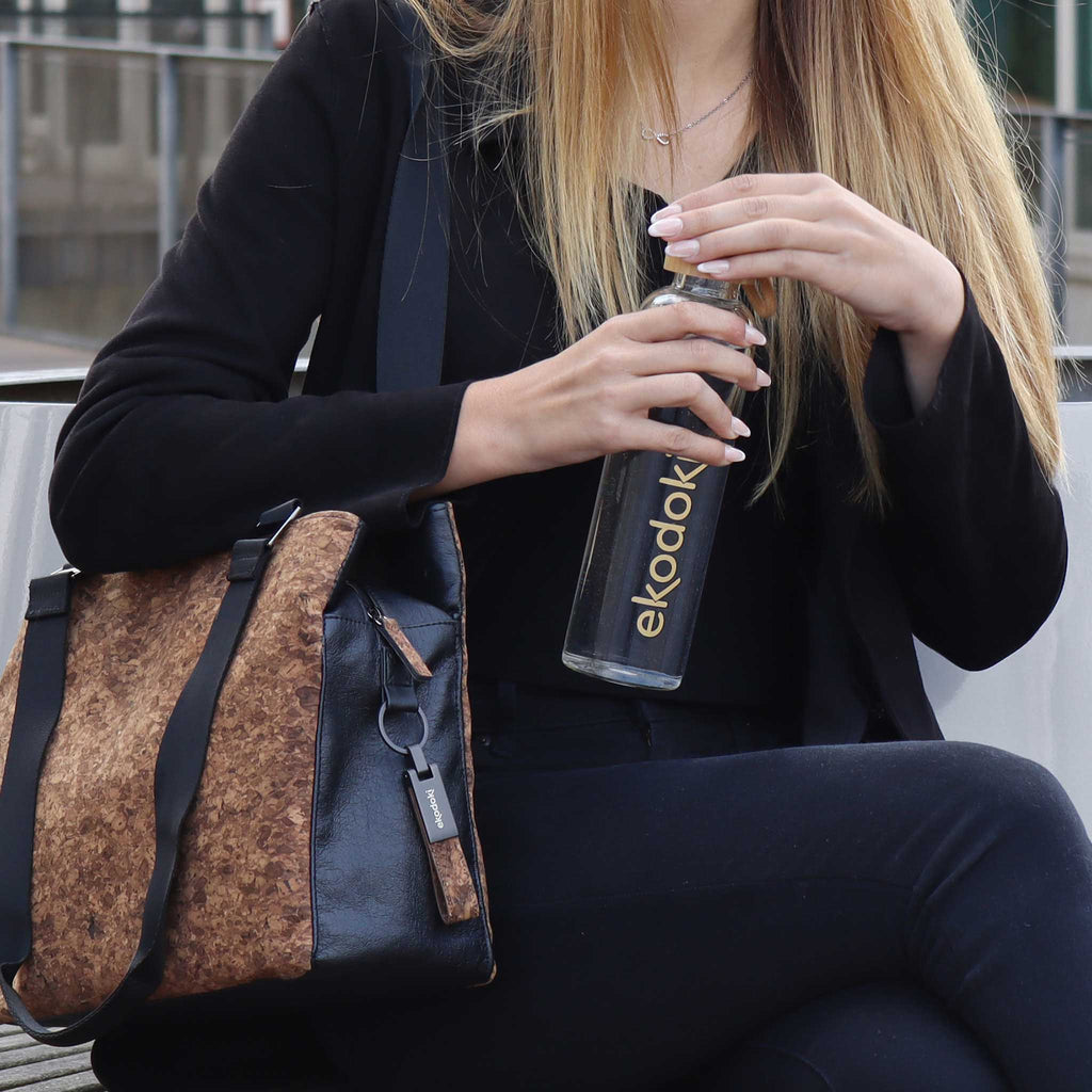 reusable glass water bottle 550ml used by female model holding it while closing the bamboo cap with her other hand eKodoKi HYDRO